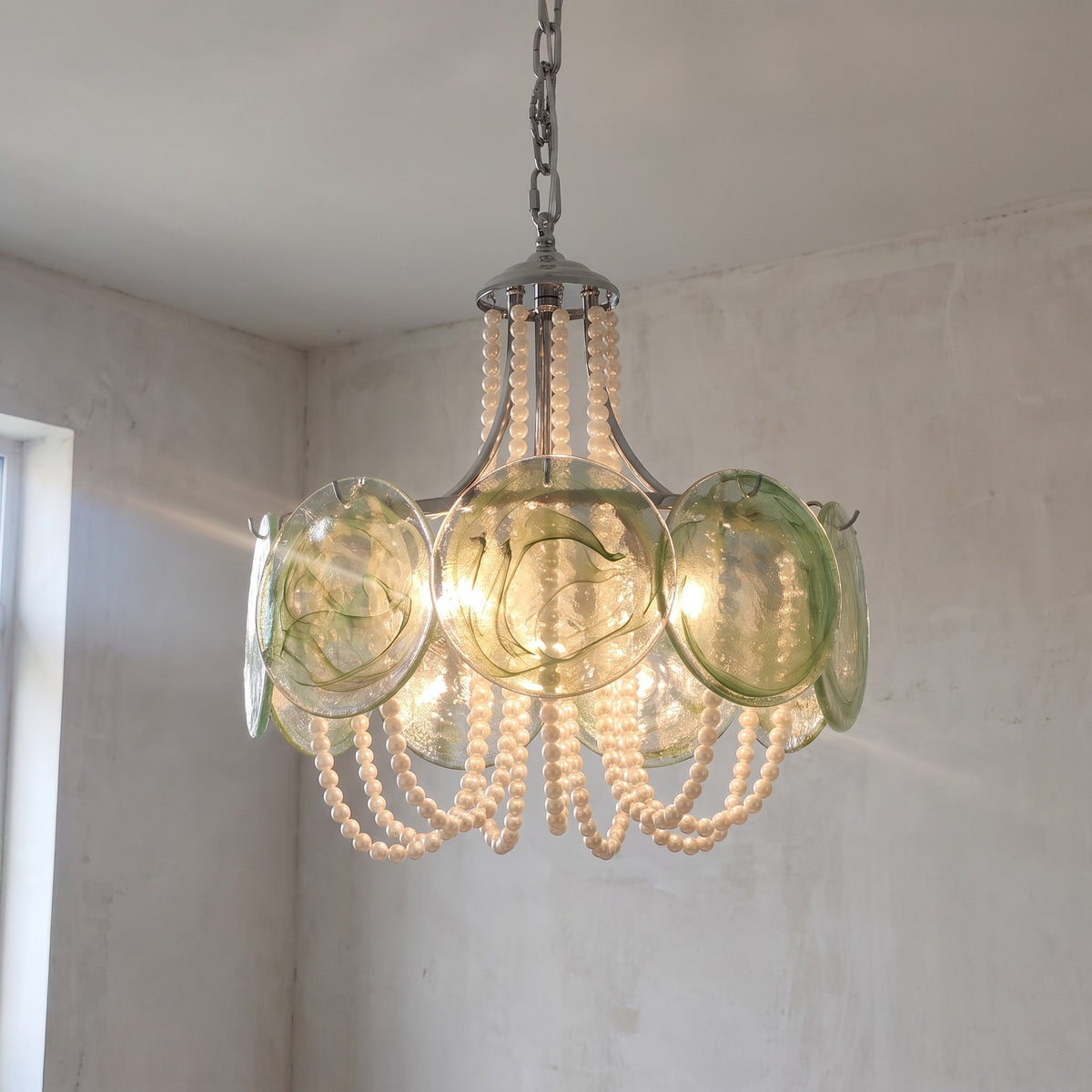 Lustre suspension style Murano vert irisé et perles, diffusant une lumière chaleureuse dans un salon moderne. Détail du verre.