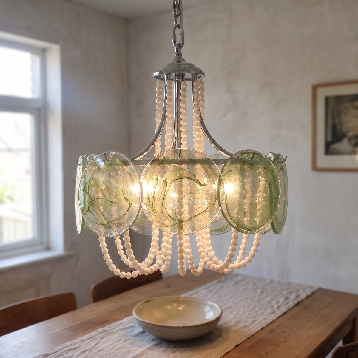Installation d'un lustre suspension style Murano vert irisé, montrant la chaîne de fixation et le support de plafond chromé.