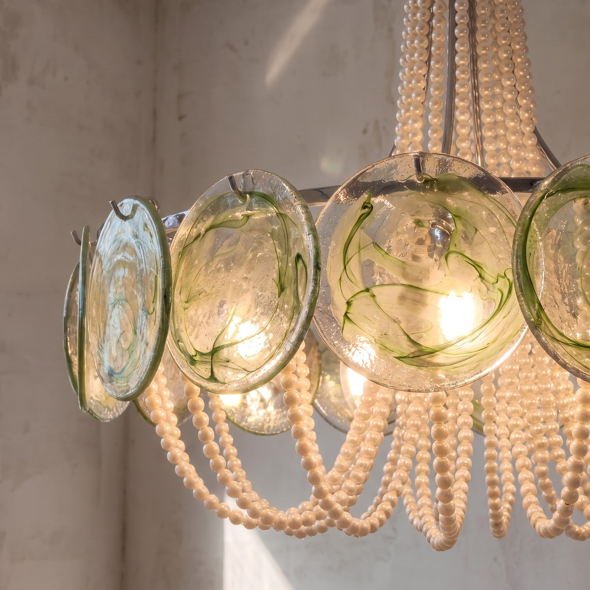 Détail des disques de verre vert pâle du lustre, mettant en valeur leur texture unique et l'éclat délicat de l'éclairage intégré.