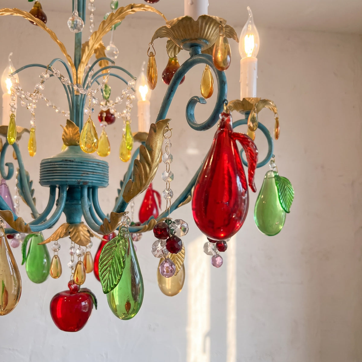 Détail rapproché des pendeloques en verre coloré (rouge, vert, violet, jaune) et de la structure métallique bleu-vert du lustre suspendu.