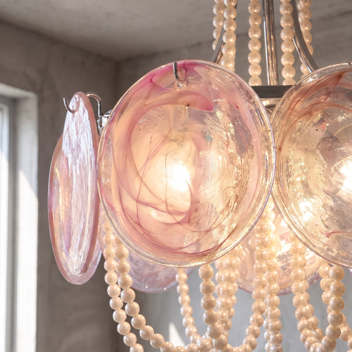 Le lustre à perles et verre rose suspendu au plafond, créant une ambiance douce et sophistiquée dans un salon contemporain.