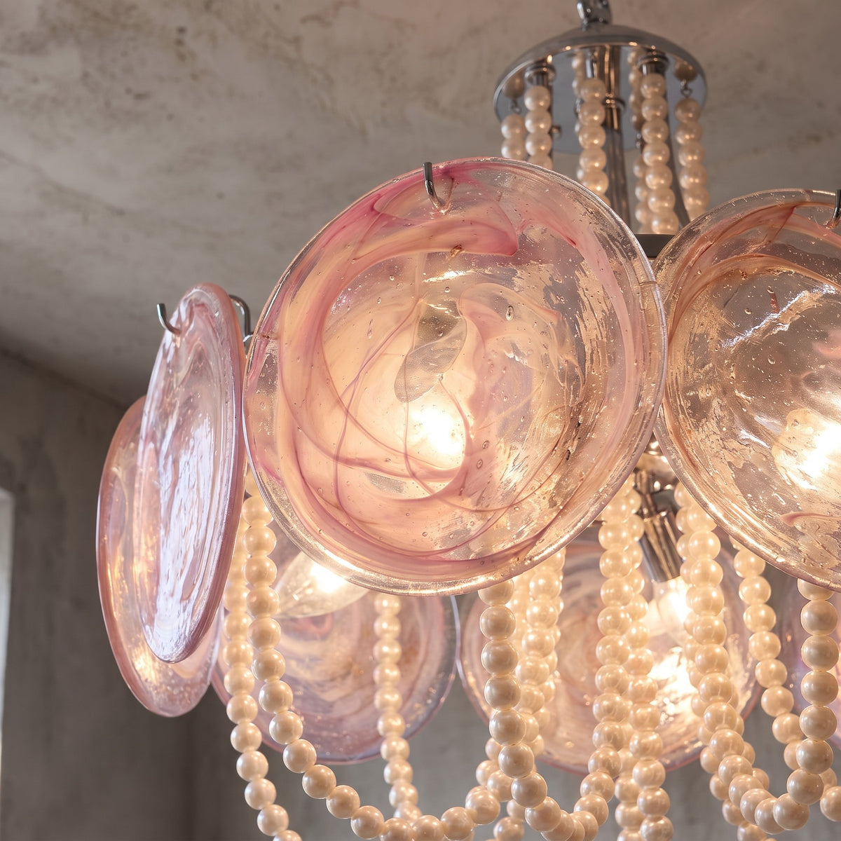 Le luminaire allumé, soulignant la chaleur de l'éclairage et la transparence du verre rose, idéal pour une salle à manger.