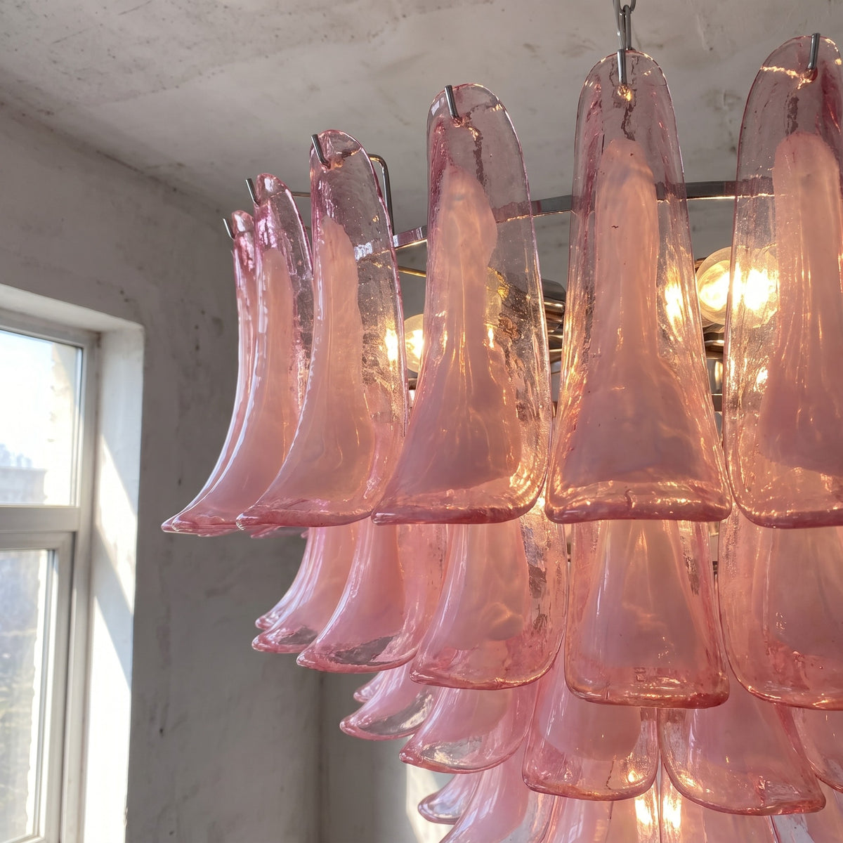 Vue latérale du lustre suspension rose, montrant les multiples niveaux de pétales de verre qui créent un effet visuel de cascade lumineuse.