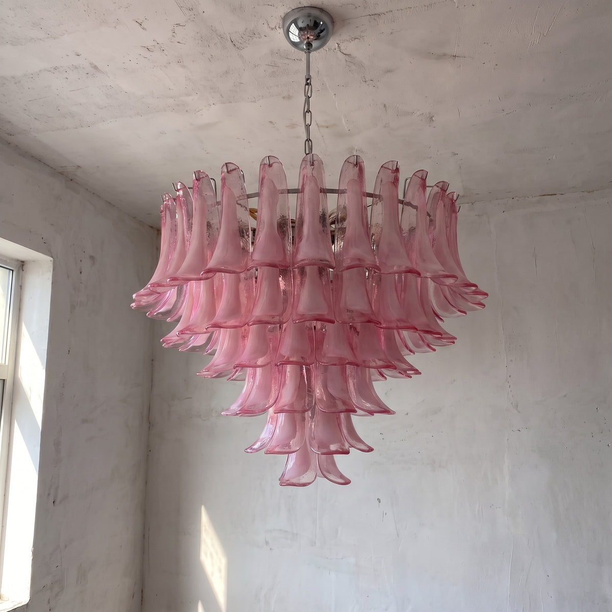 Ambiance créée par le lustre suspension en verre rose, sa lumière tamisée procurant une atmosphère relaxante et cosy dans un intérieur chic.