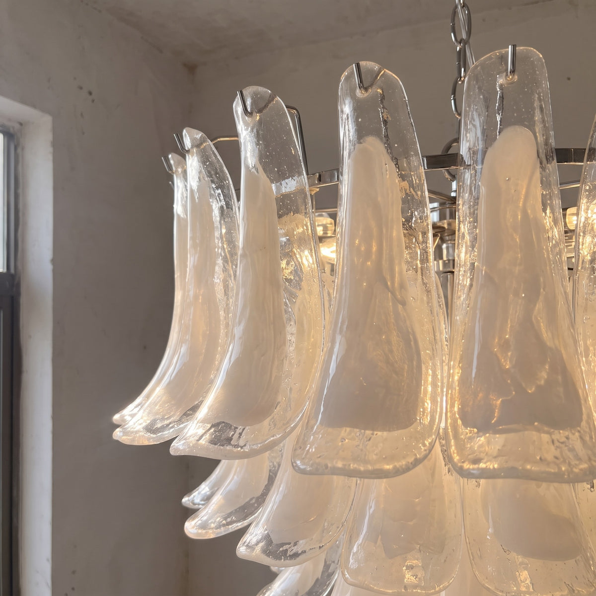 Vue rapprochée des délicats pétales de verre opalin blanc, composant ce lustre suspension inspiré de l'artisanat vénitien.