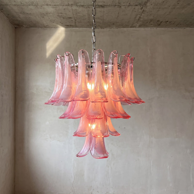 Lustre suspension en verre rose style Murano, forme pétale, éclairant un salon moderne avec une lumière douce et une élégance intemporelle.