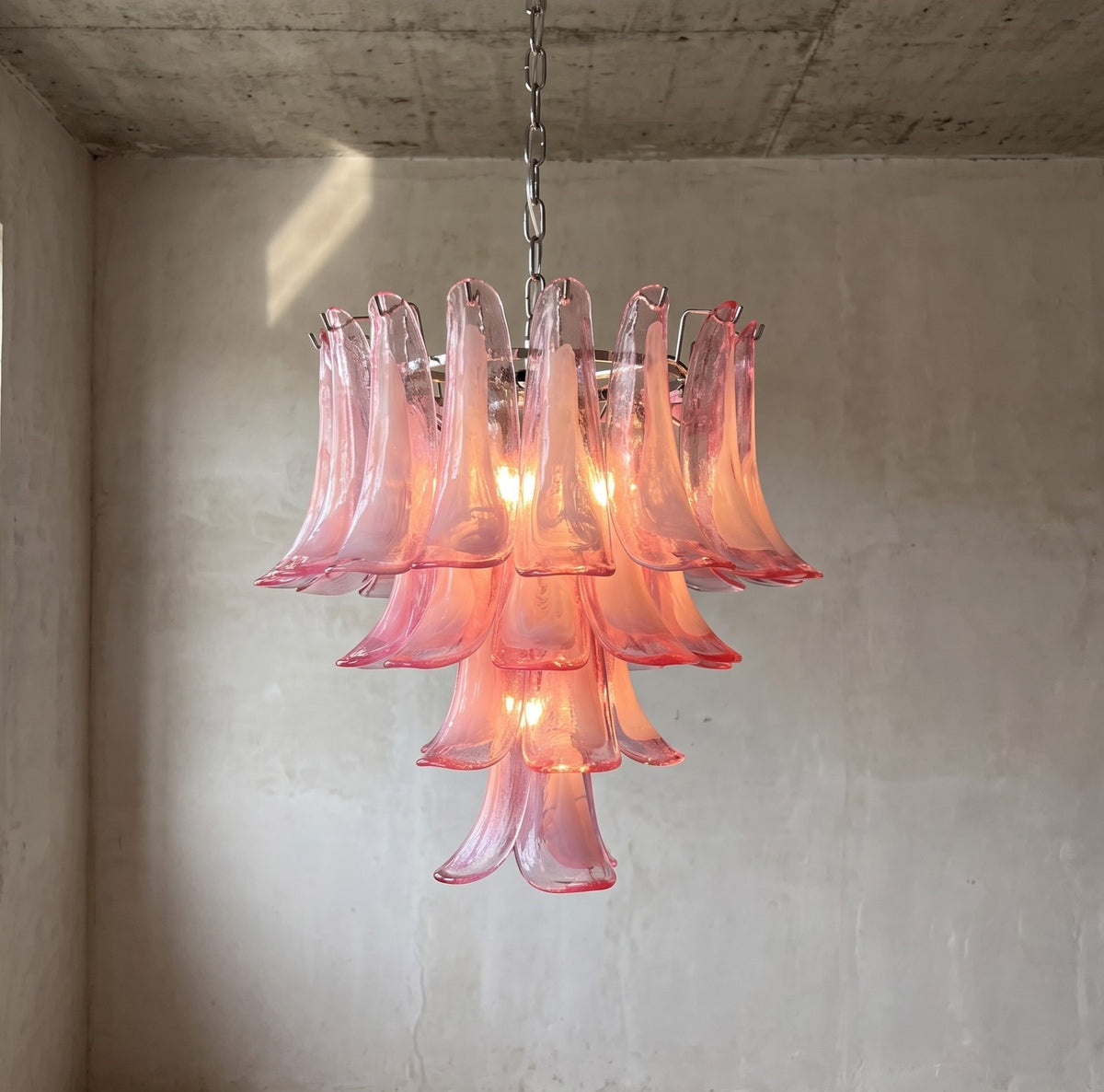 Lustre suspension en verre rose style Murano, forme pétale, éclairant un salon moderne avec une lumière douce et une élégance intemporelle.