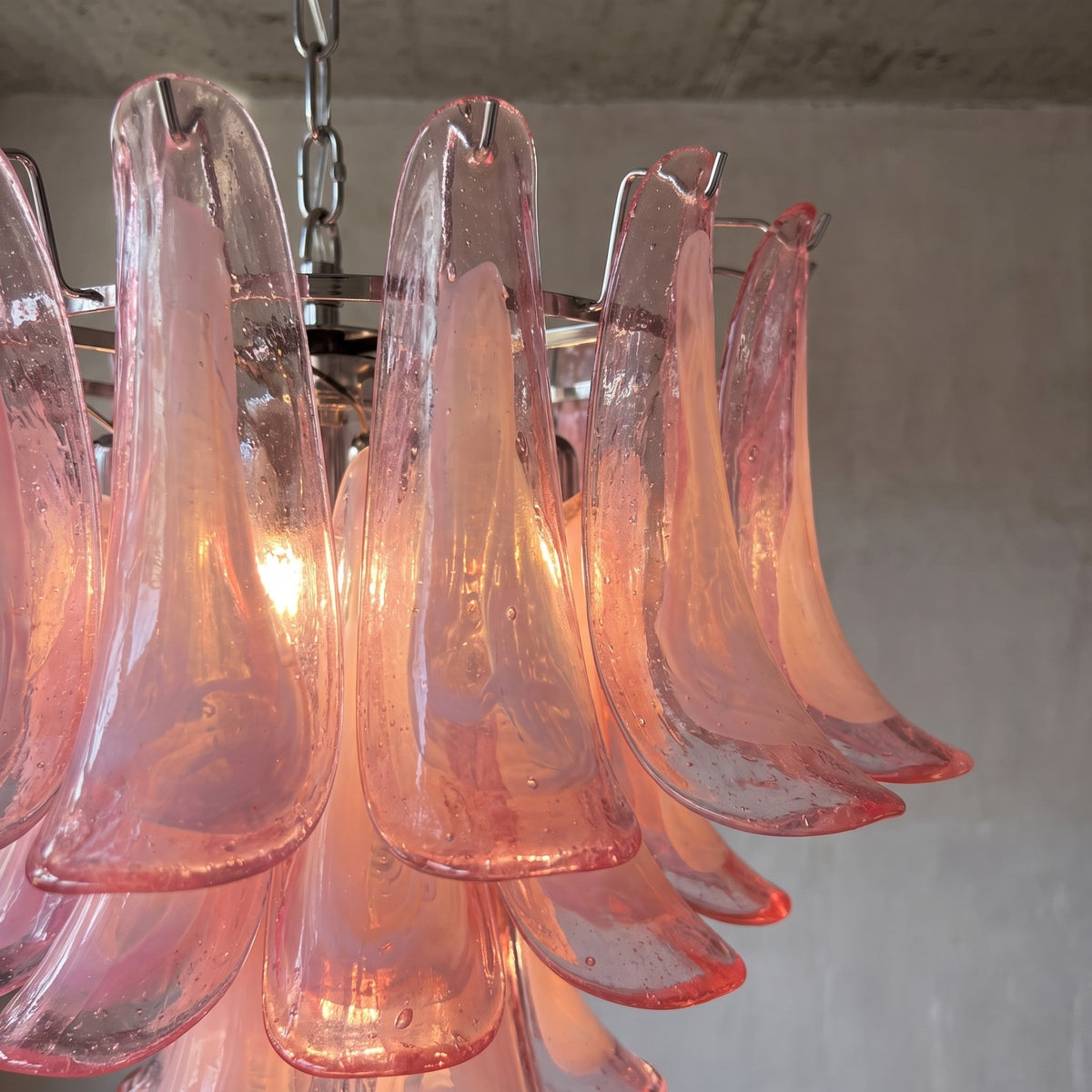 Vue rapprochée des pétales de verre rose texturé d'un lustre suspension, reflétant la lumière pour une ambiance chaleureuse et raffinée.