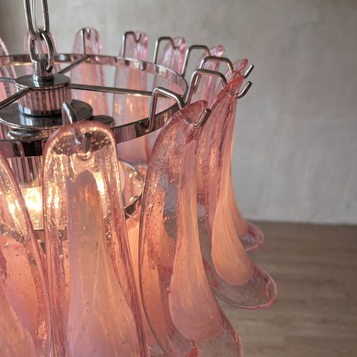 Lustre suspension en verre rose allumé, créant des reflets subtils sur les murs d'une pièce, idéal pour une ambiance cosy et élégante.