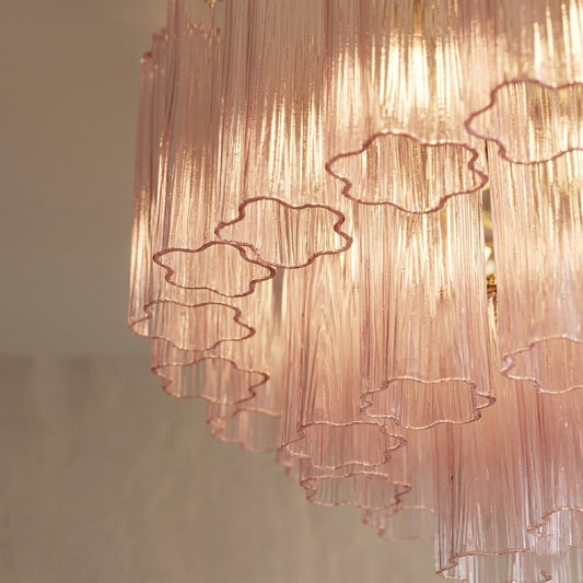 Gros plan sur les tubes de verre rose soufflé du lustre, montrant la texture délicate et la couleur sous la lumière tamisée.