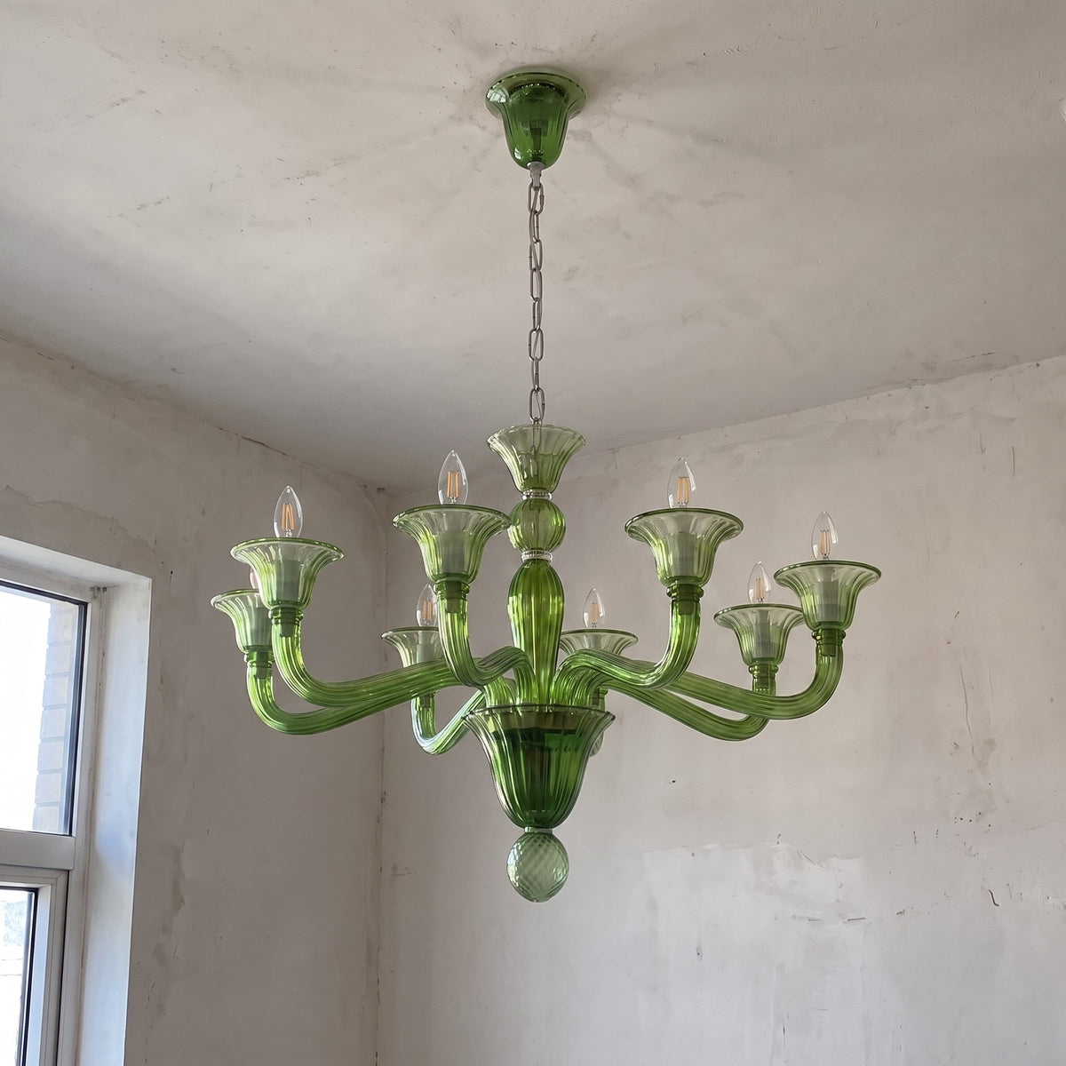 Détail des bras courbés et des coupelles en verre soufflé vert du lustre, évoquant le raffinement du style vénitien Murano.