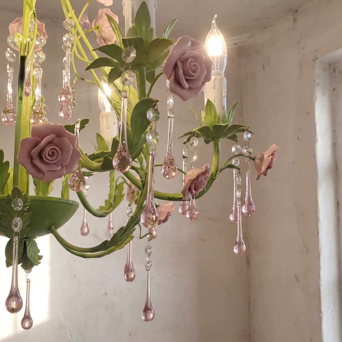 Vue d'ensemble d'un lustre romantique vert pastel, orné de roses en céramique poudrée et de pampilles de cristal délicates.