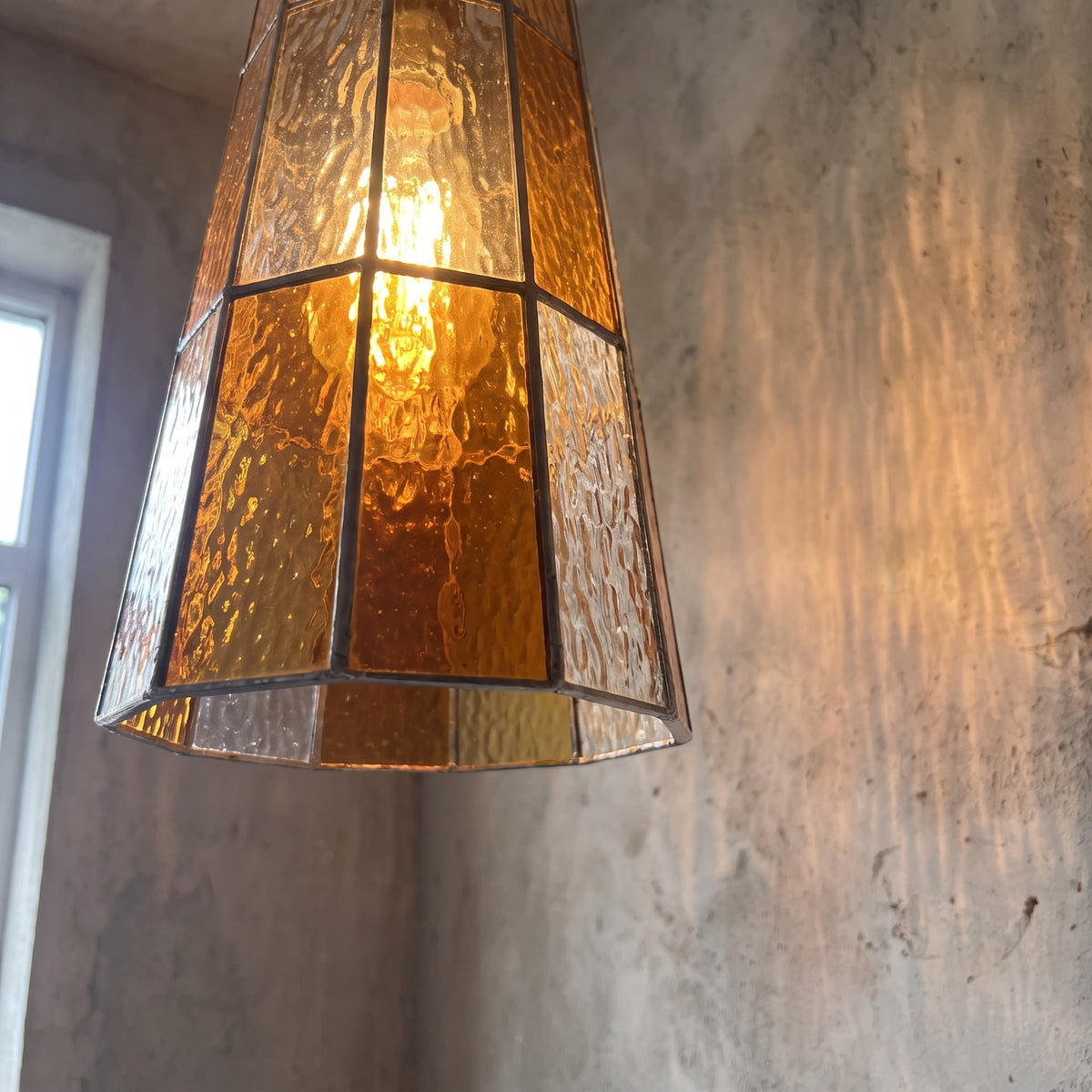 Suspension en verre orange ambré allumée, diffusant une lumière chaude et accueillante dans une cuisine moderne.