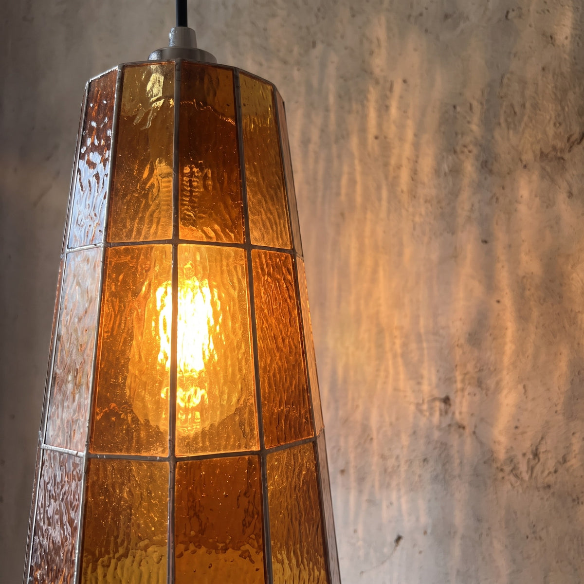 Détail des panneaux de verre teinté orange ambré de la suspension, texture unique et reflets lumineux. Style artisanal.