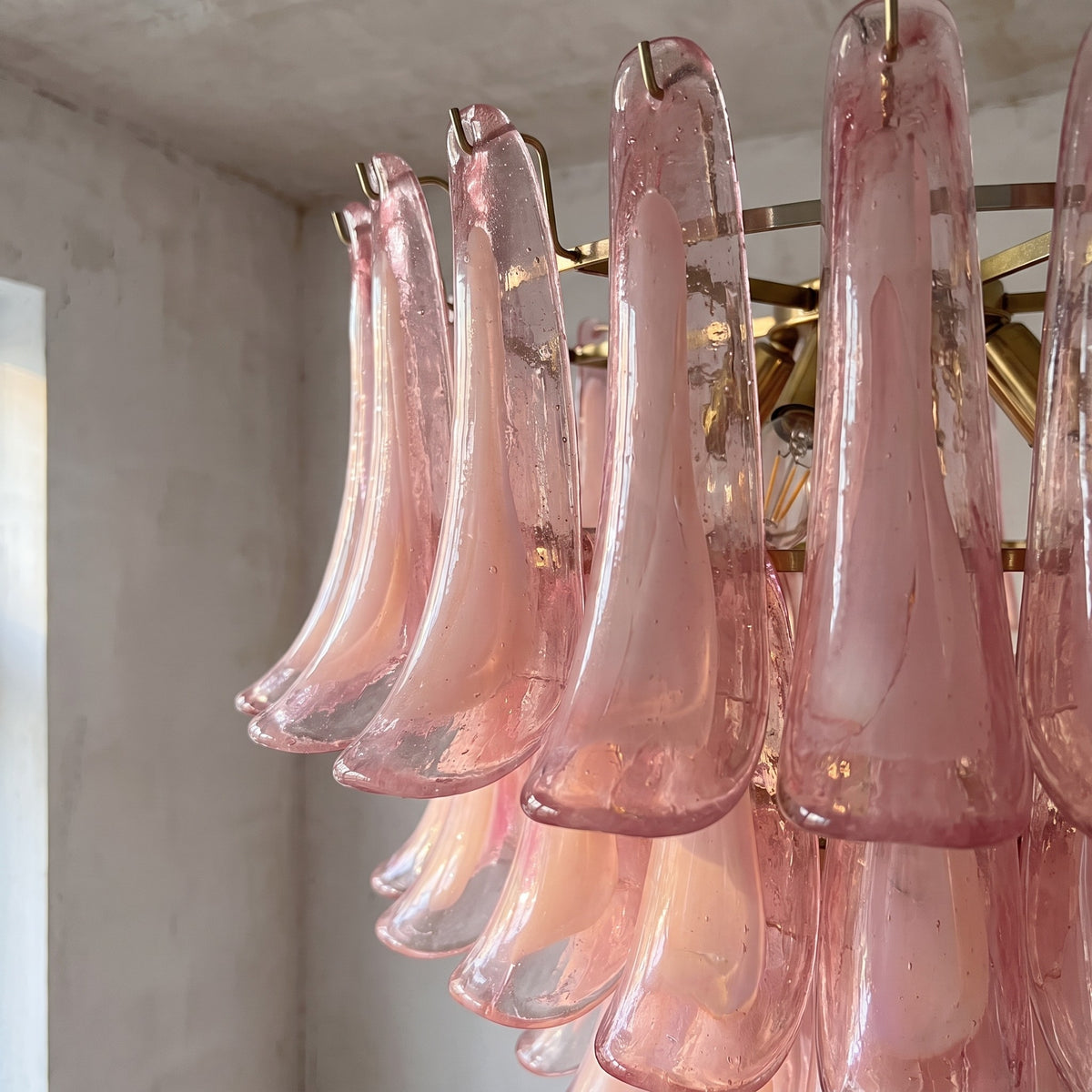 Détail rapproché des pétales en verre soufflé rose pastel du lustre, montrant la texture et la translucidité délicate du matériau.