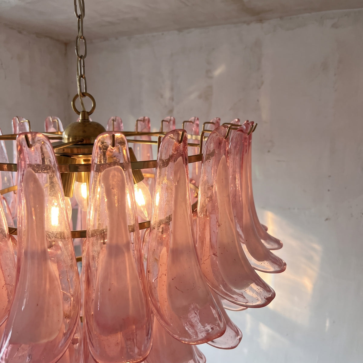Ambiance chaleureuse créée par la suspension style Murano rose allumée, diffusant une lumière douce dans une chambre principale.