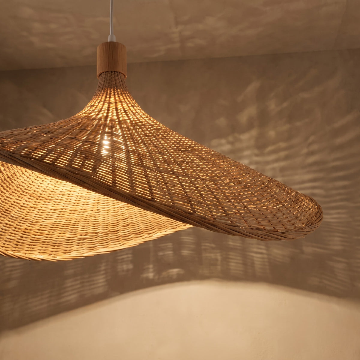 Suspension style Wabi-Sabi en rotin naturel, allumée, projetant des motifs lumineux subtils sur le plafond, créant une atmosphère relaxante.