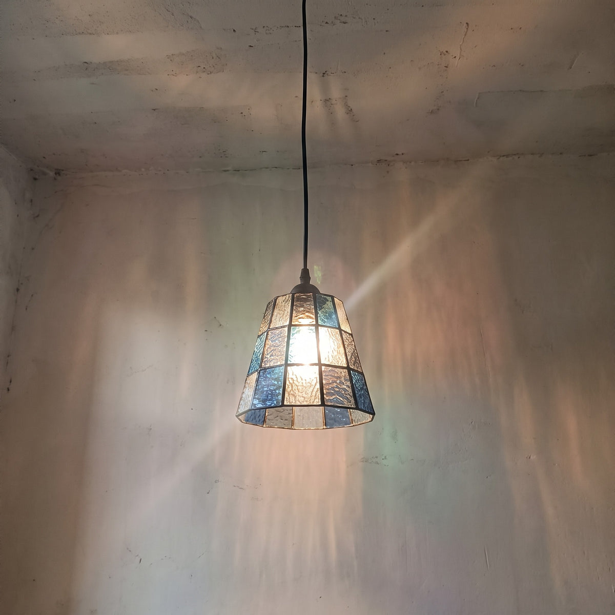 Vue rapprochée de l'abat-jour en verre texturé, montrant les nuances de bleu, d'ambré et transparentes du style Murano.