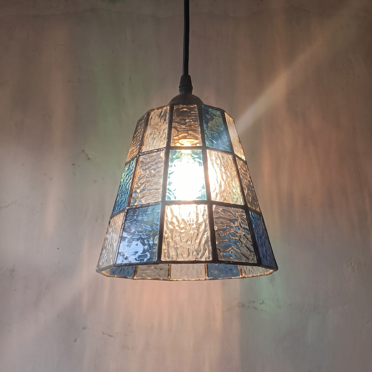 Suspension style Murano vintage en verre texturé bleu et ambré, éclairant un coin lecture avec une lumière douce et colorée.