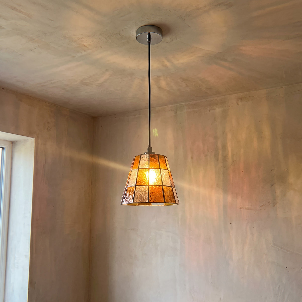 Vue d'ensemble de la suspension en verre ambré, câble noir ajustable et rosace de plafond discrète, idéale pour une cuisine ou salle à manger.