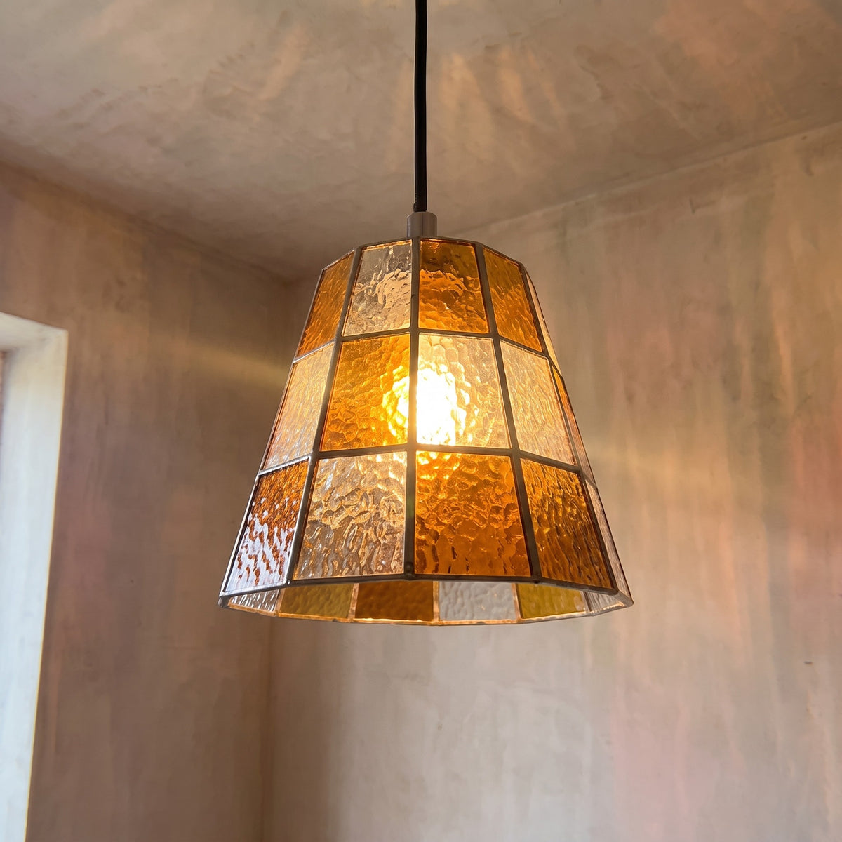 Suspension en verre ambré style Art Déco allumée, détails des panneaux texturés, créant une lumière chaleureuse pour un salon moderne.