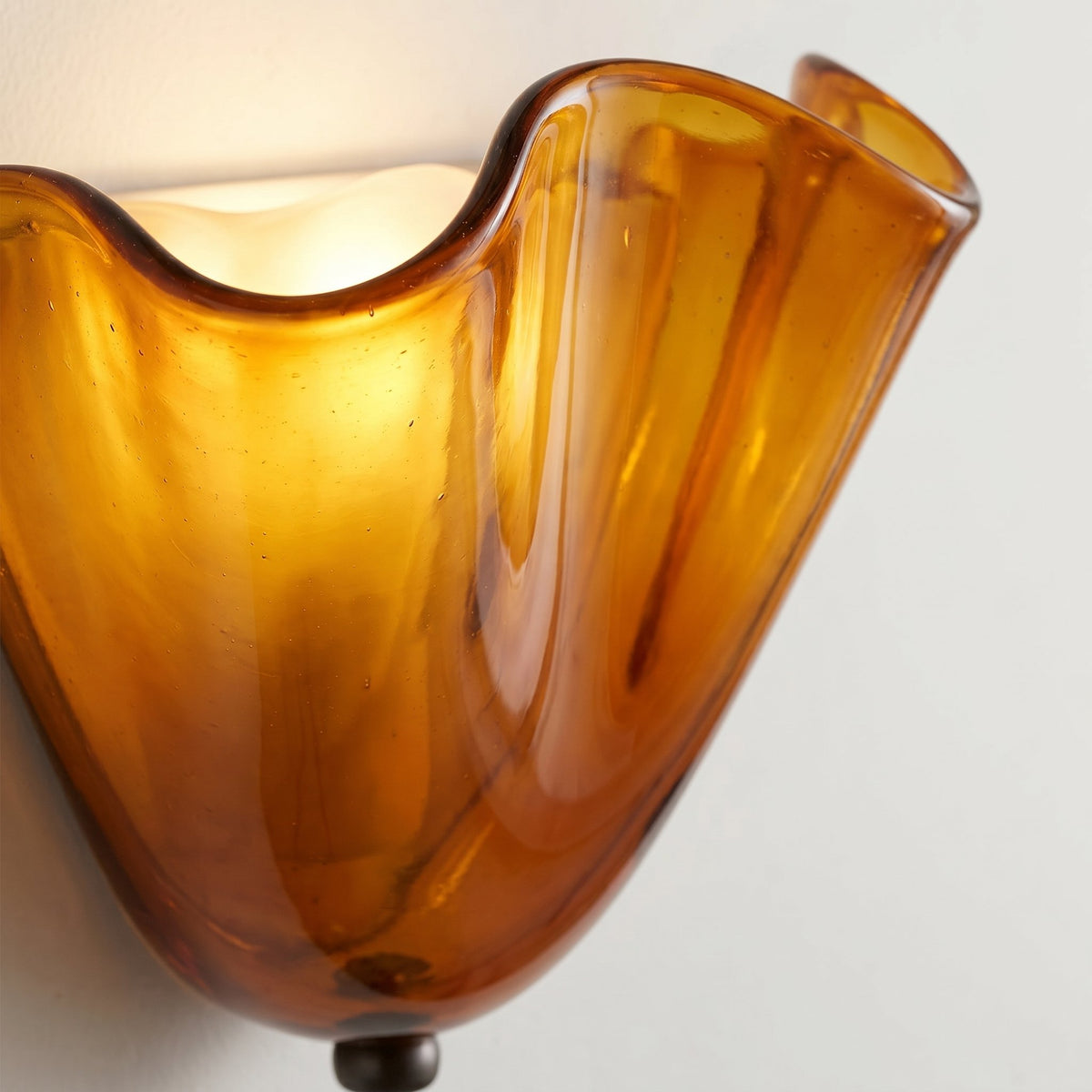 Détail de la texture et de la couleur du verre ambré de l'applique, avec ses courbes élégantes évoquant un design d'époque et l'artisanat.