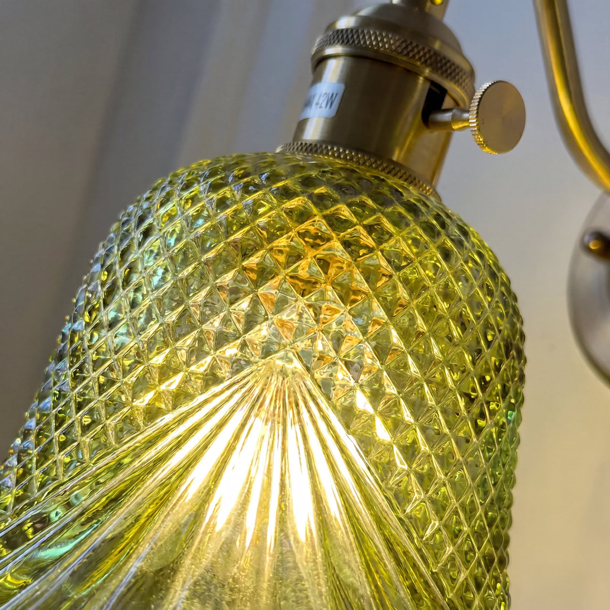 Gros plan sur la texture du verre vert de l'applique, capturant la diffusion chaleureuse de la lumière.