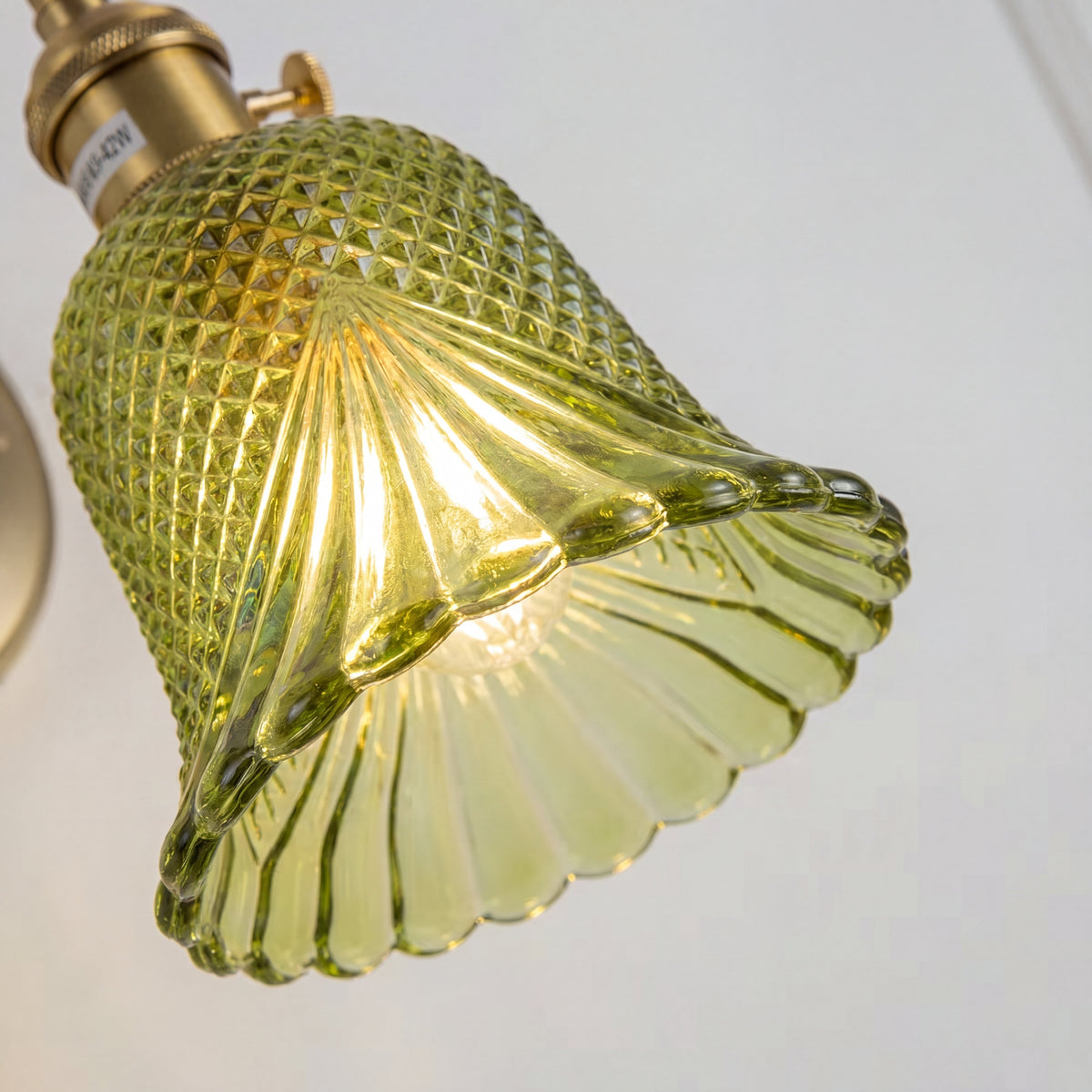 Vue détaillée de l'abat-jour en verre facetté vert de l'applique, montrant les motifs géométriques uniques.