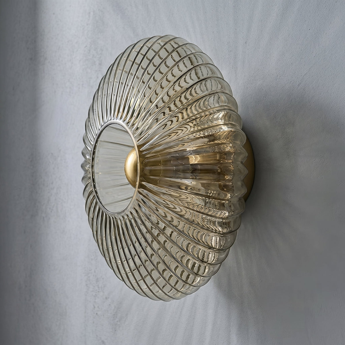 Détail de la base métallique dorée de l'applique, contrastant avec le verre cannelé gris fumé, pour une touche Art Déco élégante.