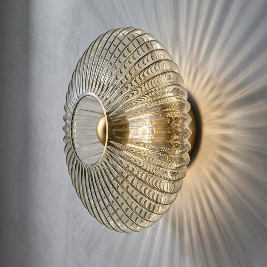 Vue d'ensemble de l'applique murale en verre cannelé gris fumé, diffusant une lumière chaude sur un mur clair, idéale pour un salon élégant.