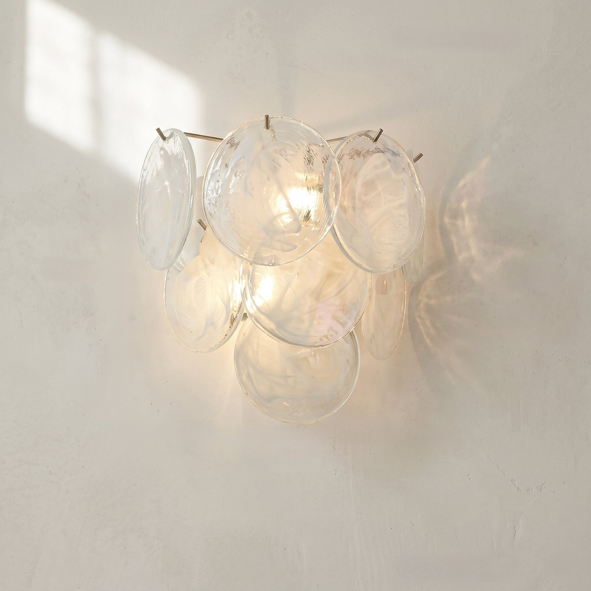 Applique murale style Murano blanc irisé éclairée, diffusant une lumière douce et chaleureuse dans une chambre moderne.