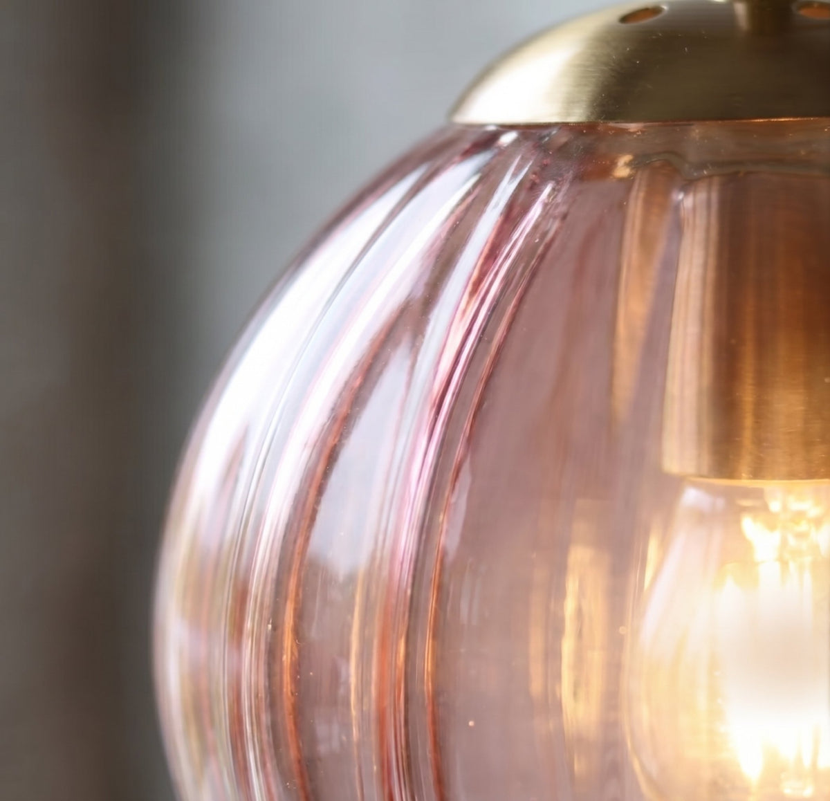Applique murale allumée, le verre teinté rose met en valeur l'ampoule E14, créant une ambiance cosy et accueillante.