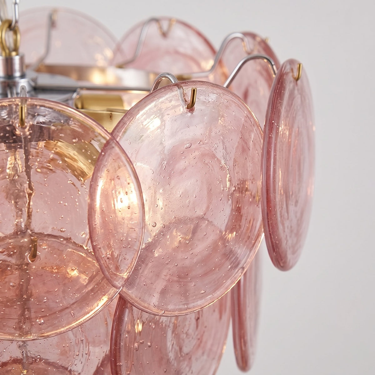 Suspension ronde de 4 niveaux en verre teinté rose, créant une ambiance élégante au-dessus d'une table de salle à manger contemporaine.