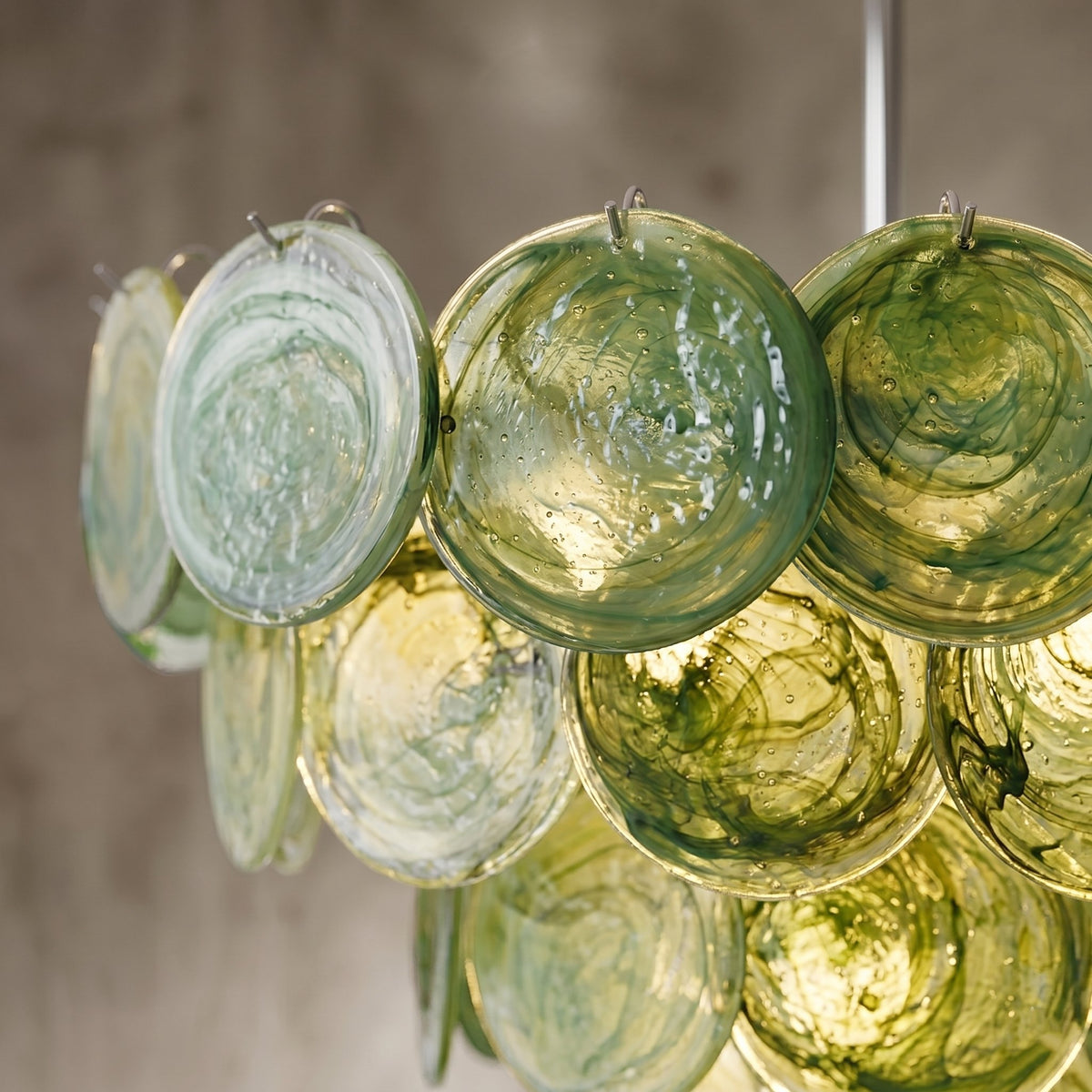 Détail rapproché des disques de verre vert teinté, révélant les nuances et la texture artisanale du lustre Murano.