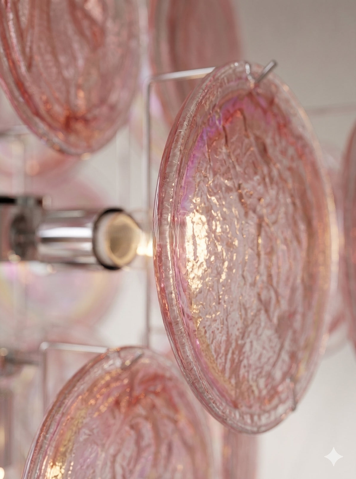 Le lustre allumé, diffusant une lumière douce et chaleureuse qui met en valeur les reflets uniques du verre irisé rose.