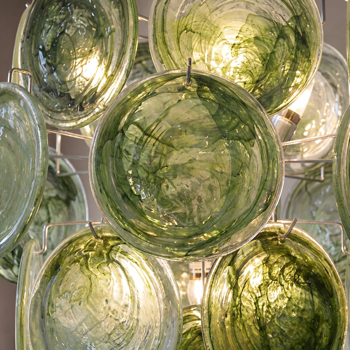 Vue rapprochée des disques de verre soufflé vert profond du lustre, révélant les motifs artistiques et la texture délicate.