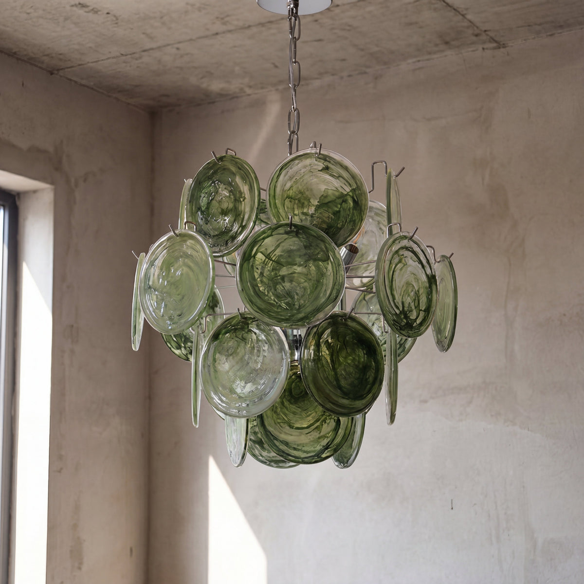 Image du lustre allumé, mettant en valeur les nuances de vert émeraude et les jeux de lumière sur les murs.