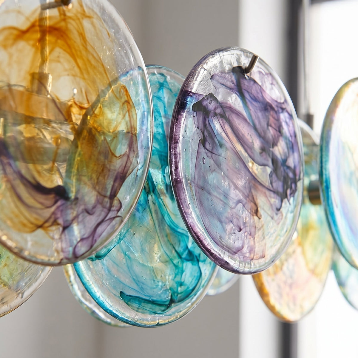 Gros plan sur la texture et les couleurs changeantes des disques de verre irisé du lustre suspension, révélant leur fabrication soignée.
