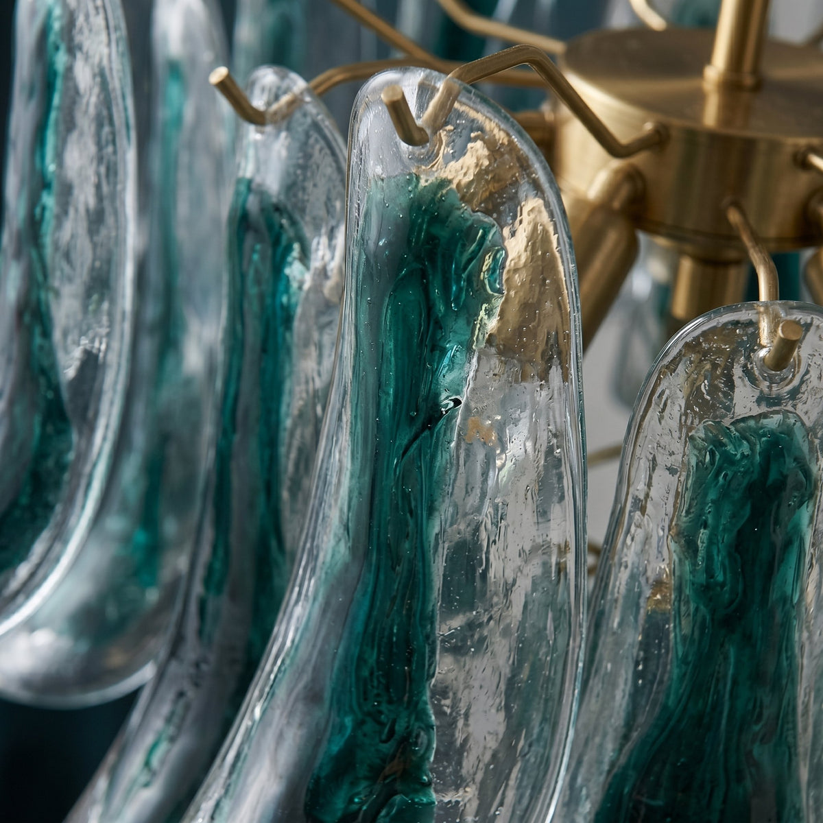 Détail rapproché des éléments en verre artisanal soufflé vert-bleu du lustre, montrant leur texture unique.