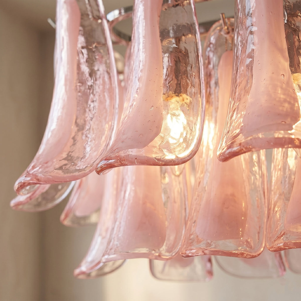 Lustre en verre rose pétale allumé, diffusant une lumière chaude et accueillante, créant une atmosphère cosy dans le salon.