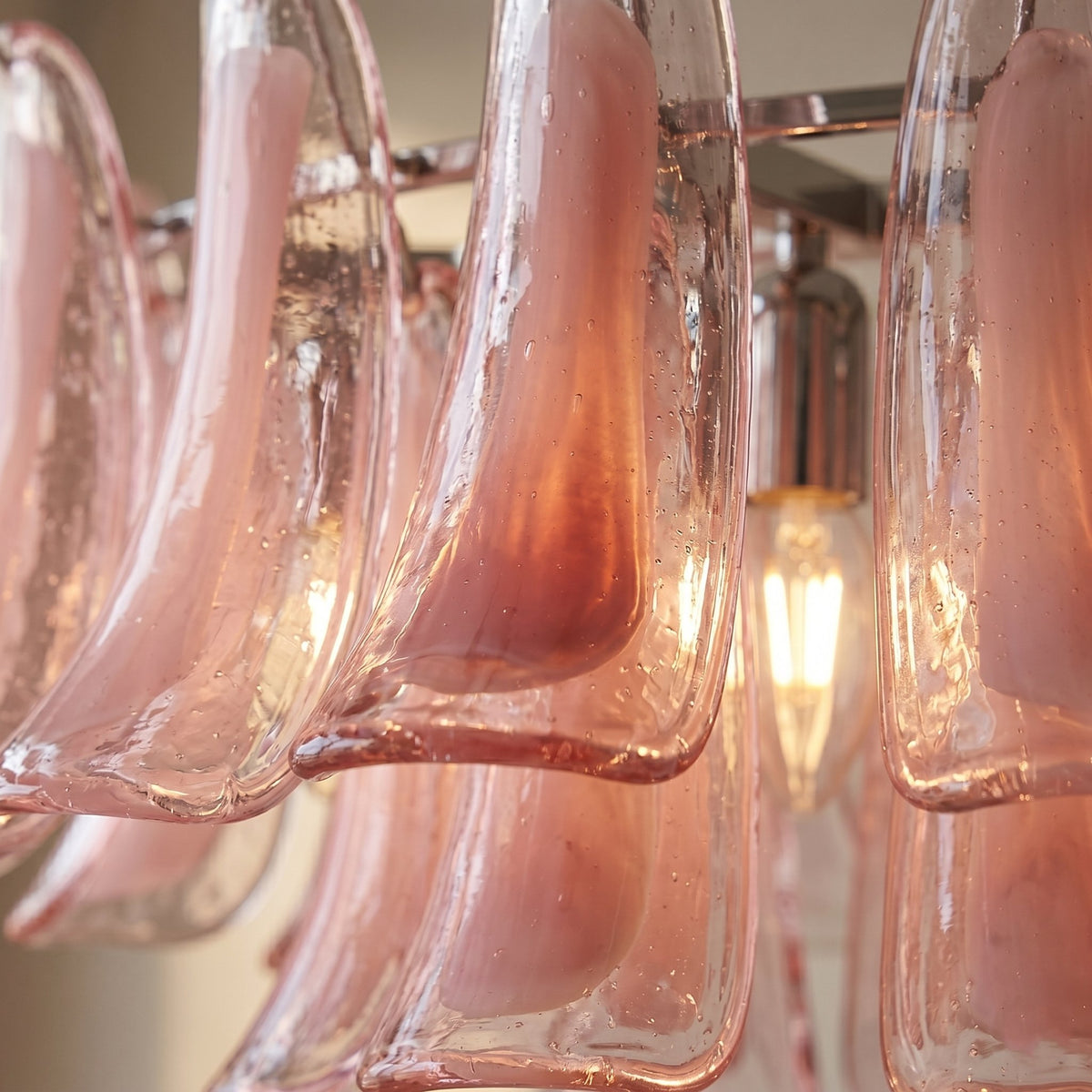 Détail de la structure en métal chromé du lustre, soutenant les éléments en verre rose avec discrétion et robustesse.