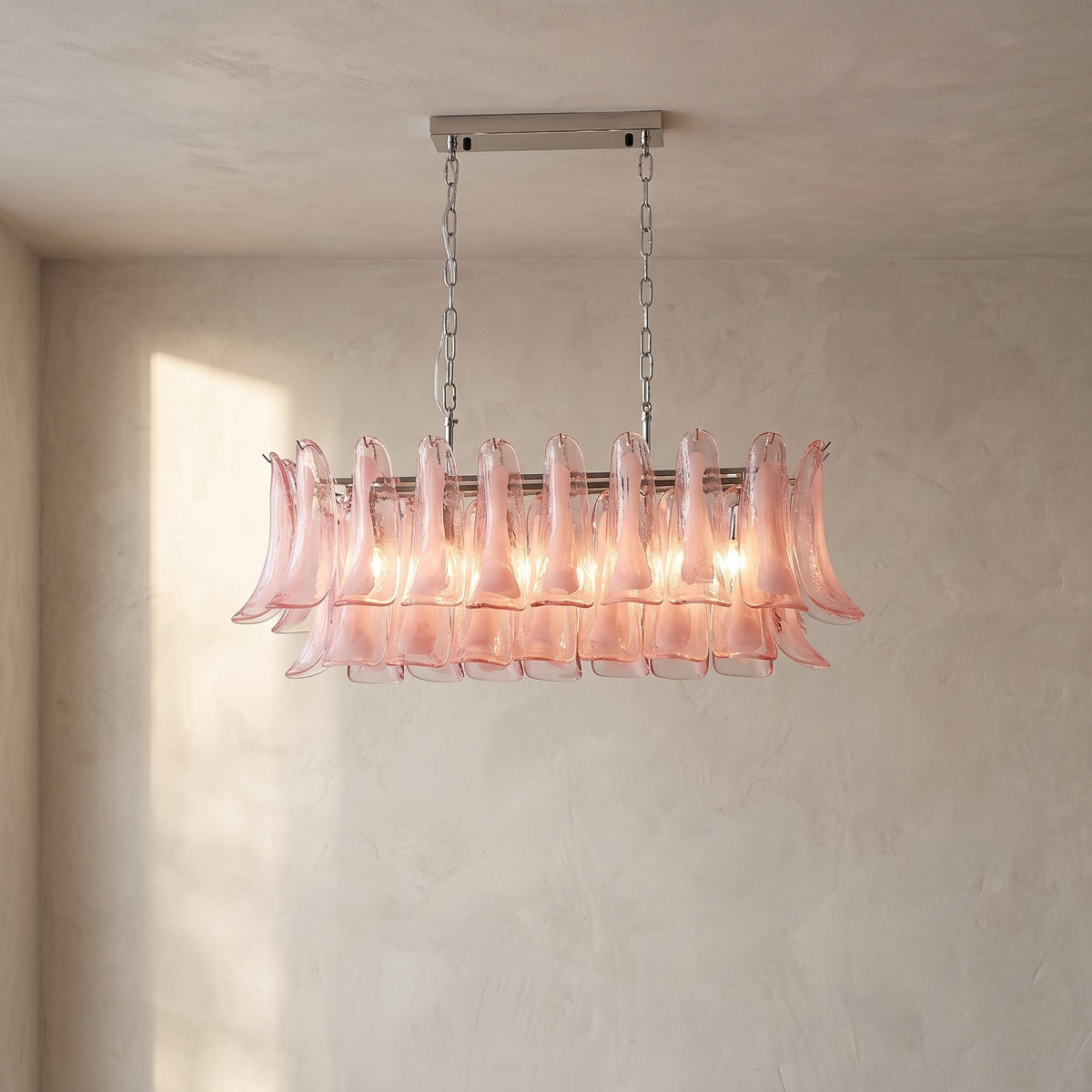 Lustre suspendu rectangulaire en verre rose pétale, illuminant une salle à manger moderne avec élégance et douceur.