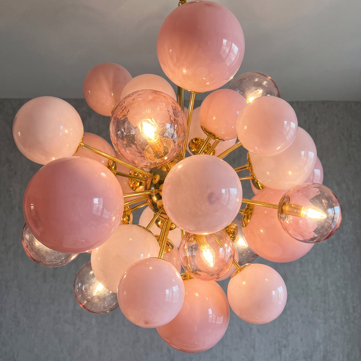 Vue rapprochée des sphères de verre rose poudré et transparentes du lustre, reflétant la lumière avec subtilité. Détail artistique.