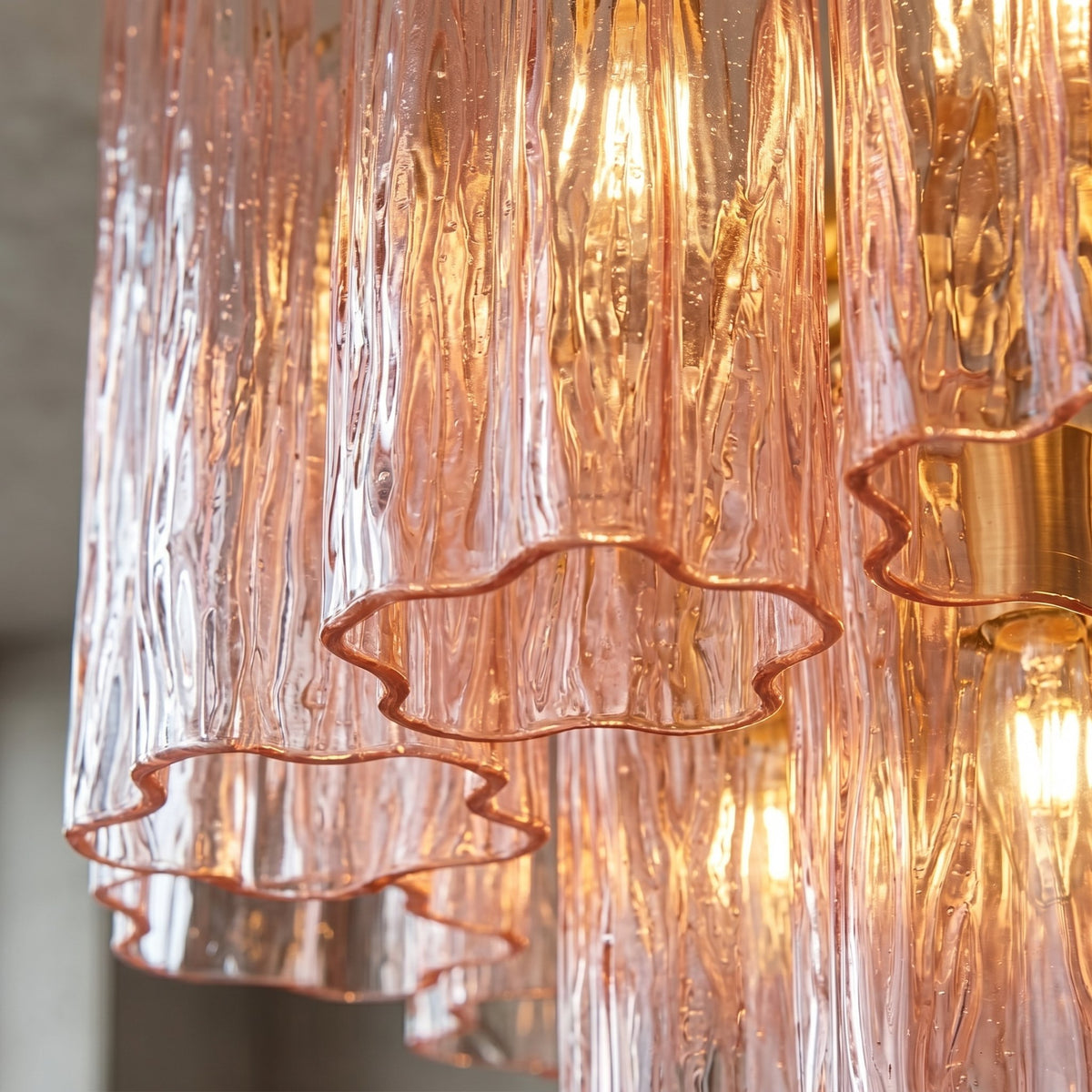 Détail du cadre métallique doré du lustre, contrastant avec le verre rose et soulignant le raffinement de l'éclairage vintage.